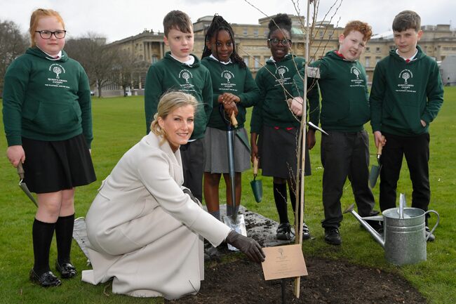 Sophie proudly posing with the planted tree and the schoolchildren who helped her